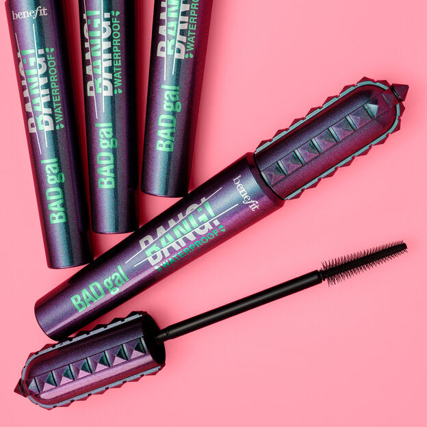 Benefit Bang! mascara tubes and the open wand on a solid pink background. The mascara packaging has a metallic purple and pink design with green text.benefit Waterproof Volumizing Mascara