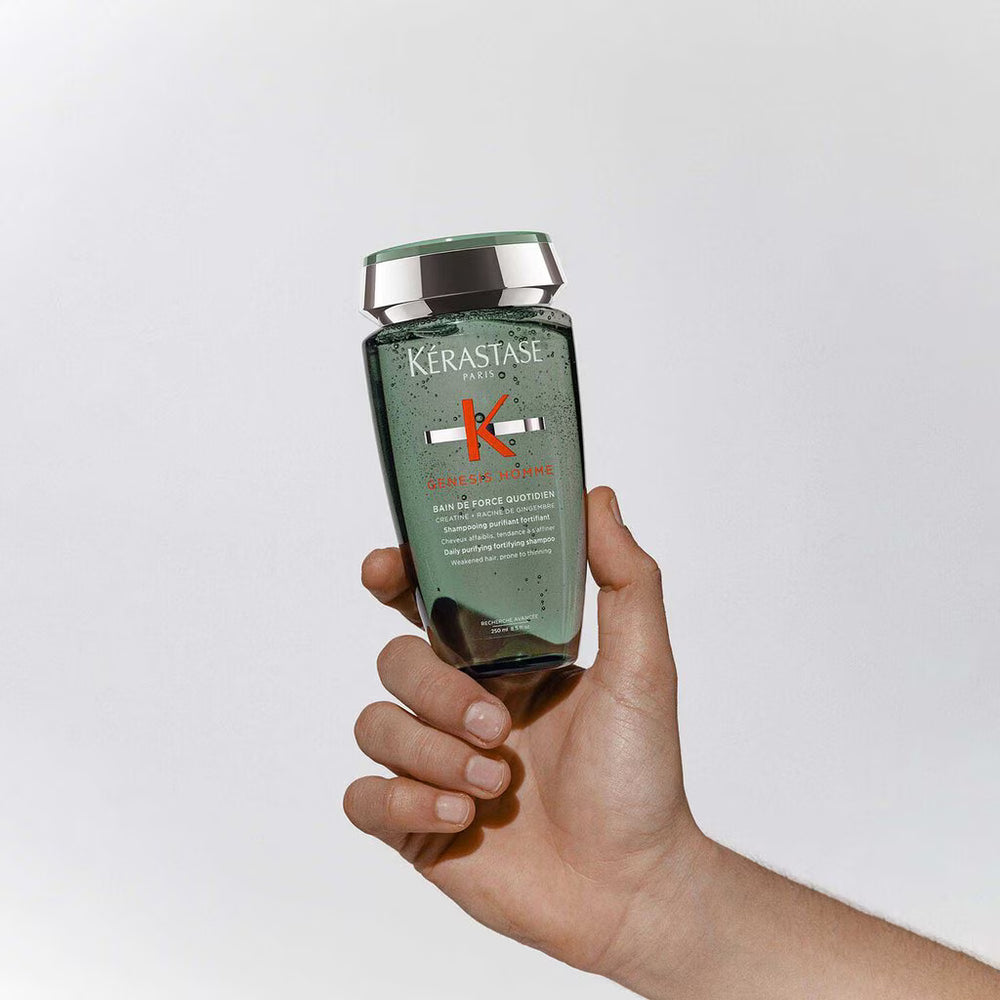 Hand holding a Kérastase bottle against a light gray background