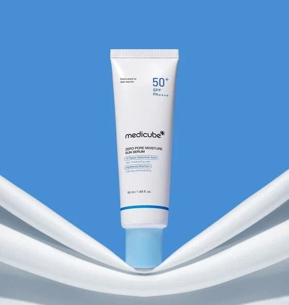 A white tube of medicube Zero-Powder Moisturizing Sunscreen SPF 50+ with a light blue cap, centered against a bright blue background with white curved graphic elements.