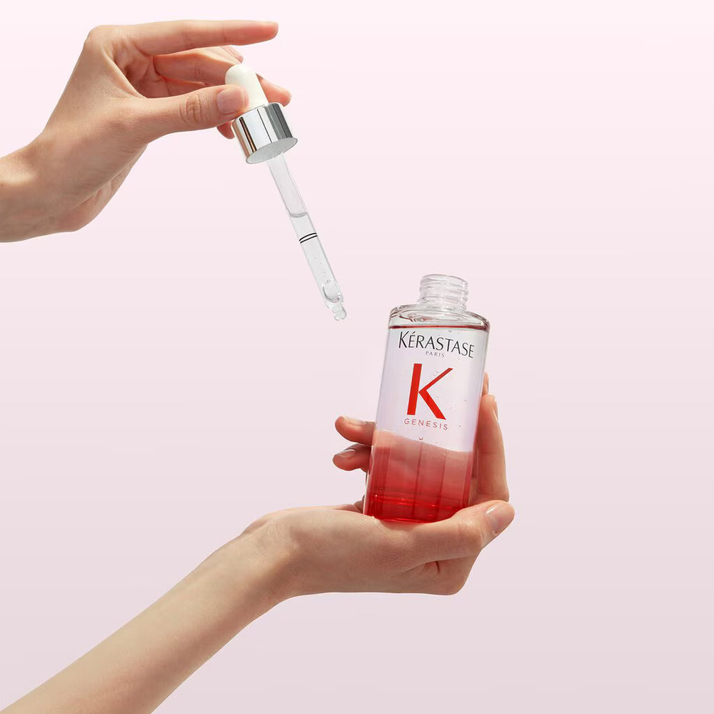 Kérastase serum bottle with dropper held by a hand on a light pink background